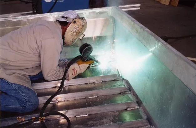 Craftsperson welding inside an aluminum boat hull at Faucheux Services